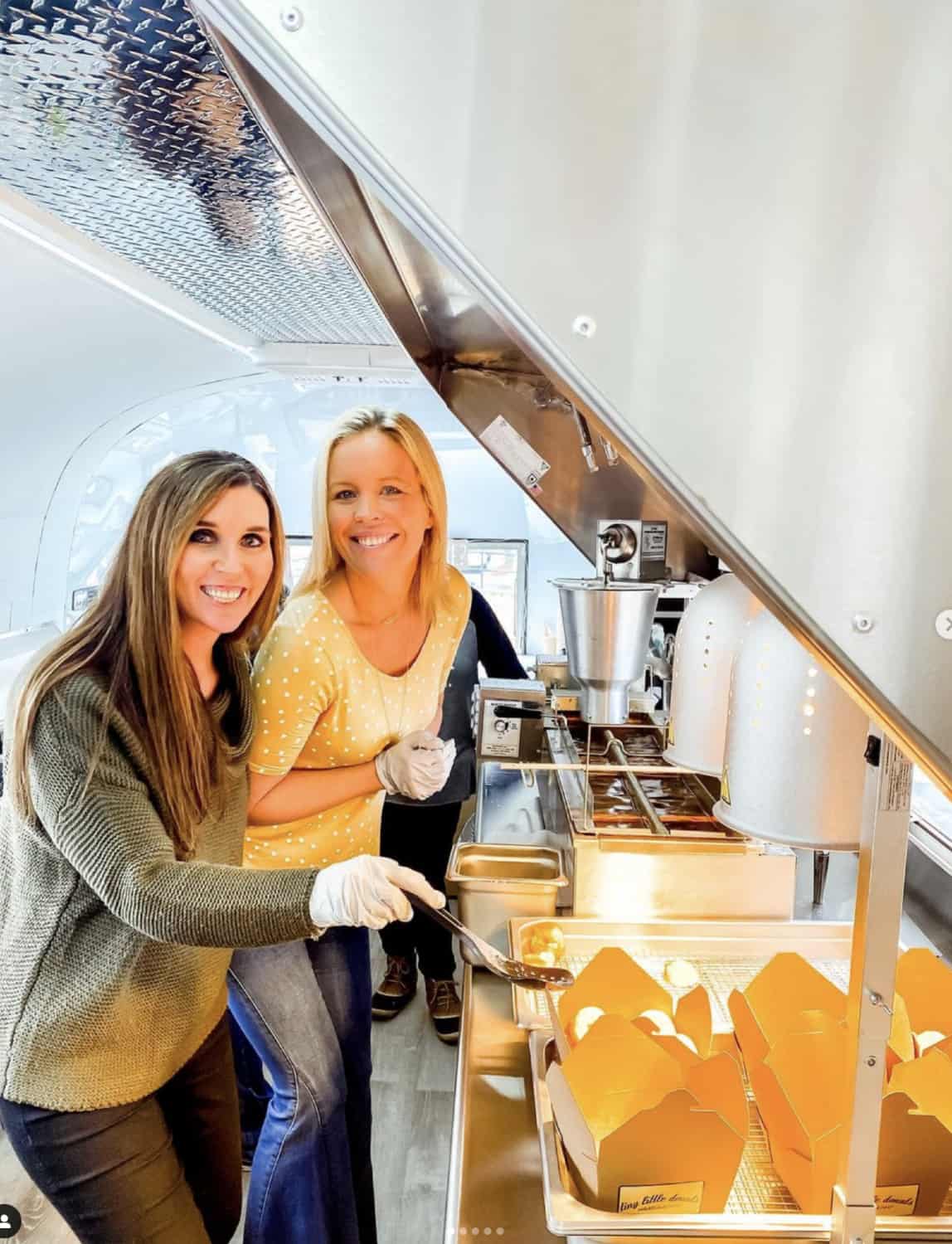 picture of two ladies on tiny little donuts kitchen poiting at the little donuts